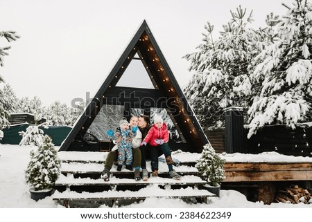 Winter holidays outdoors. Mother, father, daughter, son spend holidays at cottage. Mom, dad with child celebrate New Year. Family with kids have fun on terrace of mountain country house in snow forest