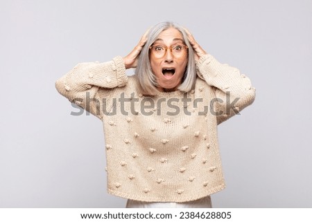 gray haired woman looking excited and surprised, open-mouthed with both hands on head, feeling like a lucky winner