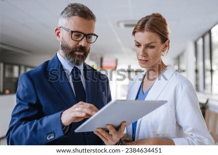 Pharmaceutical sales representative talking with female doctor in medical building. Hospital director consulting with healthcare staff. Royalty-Free Stock Photo #2384634451