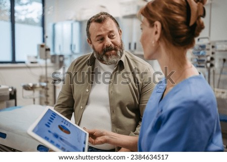 Female doctor consulting with overweight patient, discussing test result in doctor office. Obesity affecting middle-aged men's health. Concept of health risks of overwight and obesity. Royalty-Free Stock Photo #2384634517