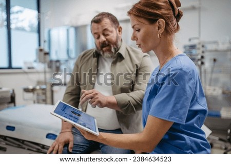 Female doctor consulting with overweight patient, discussing test result in doctor office. Obesity affecting middle-aged men's health. Concept of health risks of overwight and obesity. Royalty-Free Stock Photo #2384634523
