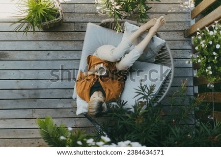 Top view of woman relaxing in the garden, drinking coffee and lying on patio chair. Mother having moment to herself while her child is sleeping.