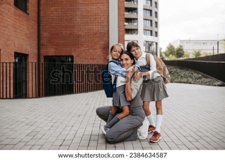 Working mother picking up daughters from school, greeting them in front of the school building. Concept of work-life balance for women. Royalty-Free Stock Photo #2384634587