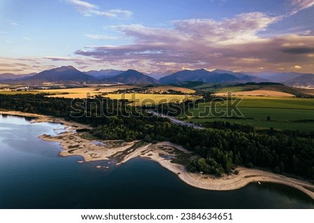 Aerial view from above the water surface of Liptovska Mara water reservoir on serene nature landscape, the Low Tatras in the distance.