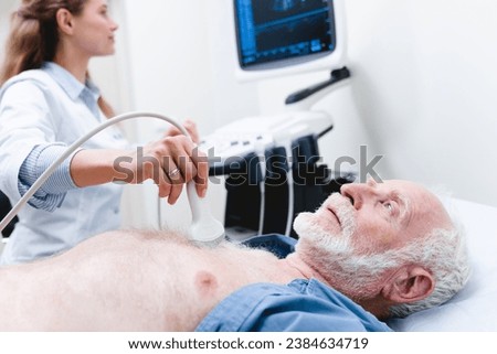 Elderly male patient undergoing examination chest by female doctor with ultrasonography device. Hospital equipment. Heart cardio illnesses. Sonographer specialist Royalty-Free Stock Photo #2384634719