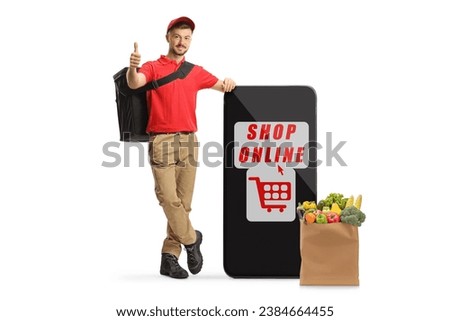 Delivery man leaning on a smartphone and a grocery bag and giving thumbs up isolated on white background