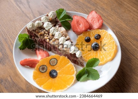 Plate with a piece of wholefood cherry cake. two cute bunny faces made of fruit. decorated with strawberry leaves. wooden background Royalty-Free Stock Photo #2384664469