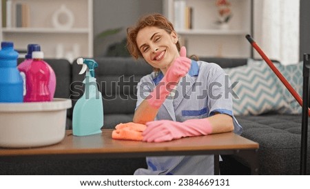 Young woman professional cleaner cleaning table doing thumb up gesture at home