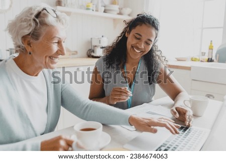 Side view of young black female volunteer social worker teaching senior caucasian lady how to use laptop, wireless internet, browsing web pages, reading news, showing her new skills Royalty-Free Stock Photo #2384674063