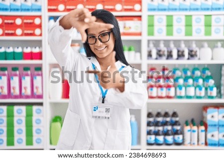 Hispanic woman working at pharmacy drugstore smiling making frame with hands and fingers with happy face. creativity and photography concept. 