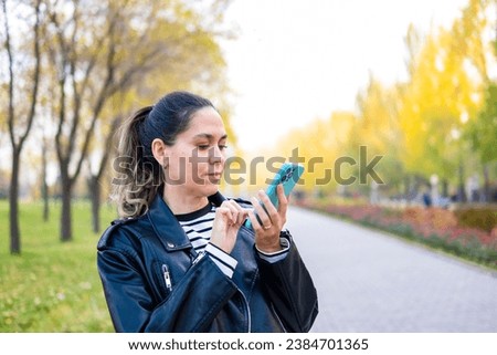 A young woman uses a smartphone in the park. A woman presses the screen of a smartphone.