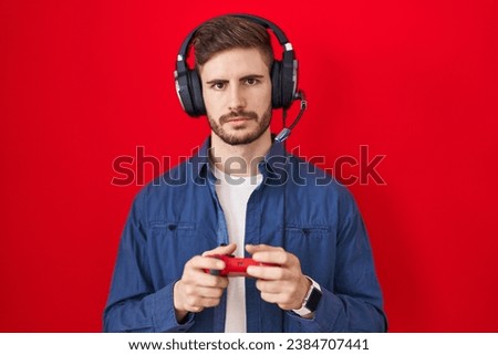 Hispanic man with beard playing video game holding controller thinking attitude and sober expression looking self confident 