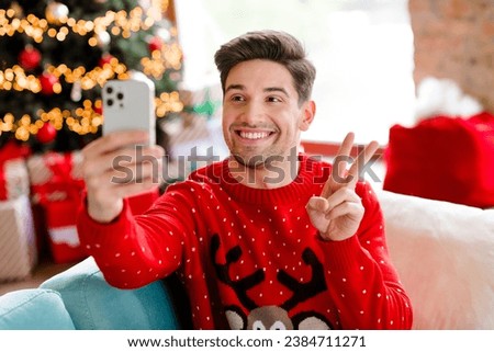 Portrait of positive handsome guy sit comfort couch make selfie demonstrate v-sign enjoy x-mas noel house indoors