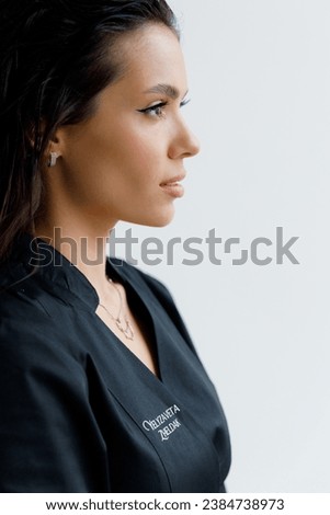 Beautiful girl in a professional work suit and apron, hair stylist and hair coloring with scissors and a comb, content shooting in a white photo studio