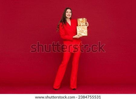 attractive woman in red tuxedo suit celebrating Christmas on red background with golden present box happy smiling long hair stylish fashion trend sale