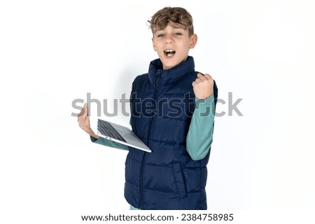 Handsome Caucasian boy wearing denim jacket hold computer open mouth rise fist