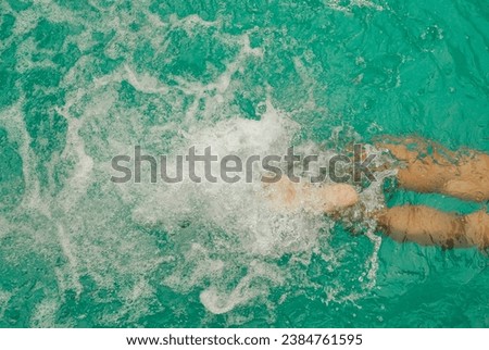 Man's legs in swimming pool. Top view shot of lower body part of the man swimming in the blue water. Feet splashing in the swimming pool. Vacation and summertime Royalty-Free Stock Photo #2384761595