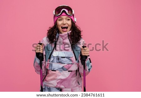 attractive smiling woman posing on pink background with skis in snow winter skiing sport suit, wearing colorful sportswear, knitted hat, glasses, concept isolated holding ski poles
