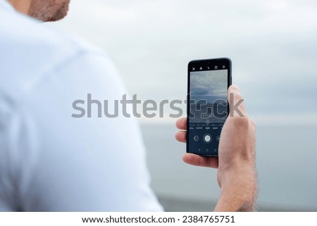 Close-up of a man's hand taking a picture of the sea and sandy beach on his phone