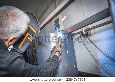 A man welder in work clothes, construction gloves and a welding mask is welded with a welding machine metal product table, Workshop near Kocani Macedonia