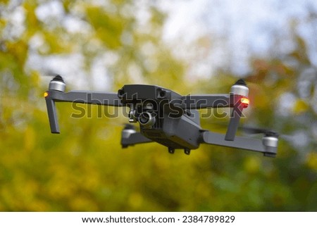 Drone quadcopter with digital camera and fast rotating propellers flying taking video and pictures. Greenery backgroud
