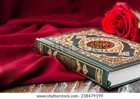 Quran - holly book of Islam with rose and red scarf on wooden background. Selective focus