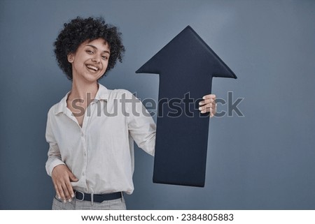 a girl on a gray background smiles, holds a black arrow in her hands, points to the top