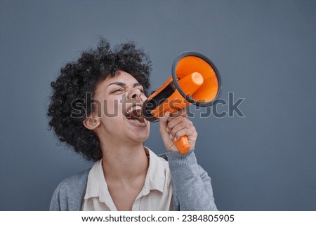 a girl on a gray background holds a loudspeaker in her hand. screams