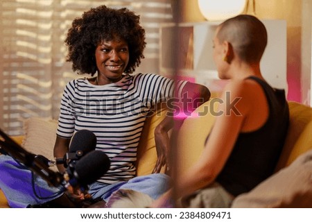 African american woman host streaming her audio podcast and using microphones at her small broadcast studio while talking to her female guest. Multiracial women radio presenters. Copy space.