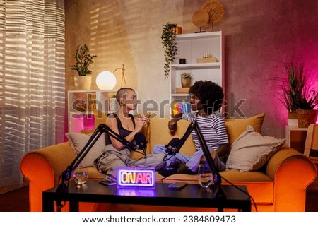 Portrait of a multiracial female radio presenters having a conversation about feminine topics in a home studio. Two diverse women recording an internet podcast for their social media channel. Royalty-Free Stock Photo #2384809473