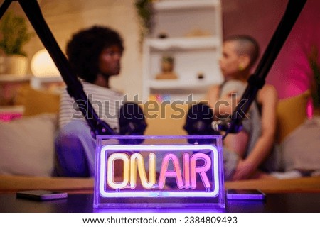 Live online radio studio desk with on air neon sign with a diverse radio presenters in the background. Entertainment and communication concept. Copy space.