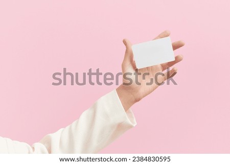 Womans hand touch a white blank business card that floats on a pink background. Flat lay of a simple business card with top view