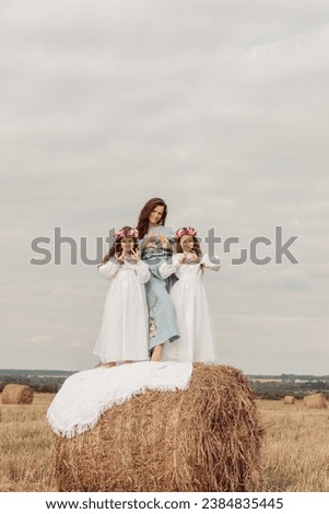 Mother and daughters are standing in the middle of the field on a pile of hay. They show their heart with their hands. Photoshoot. Family.