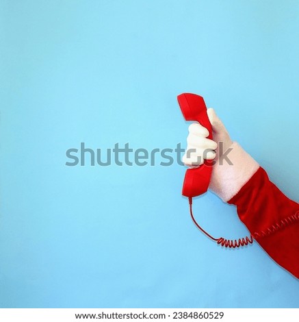 Santa Claus's hand holds a red retro telephone receiver. Telephone communication, New Year greetings, customer support concept. Copy space. Close-up. Royalty-Free Stock Photo #2384860529