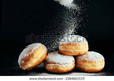 Powdered sugar is poured onto donuts. Traditional Jewish dessert Sufganiyot on black background. Celebrating Judaism holiday. Cooking fried Berliners.