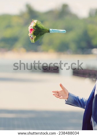 groom throwing wedding bouquet in park