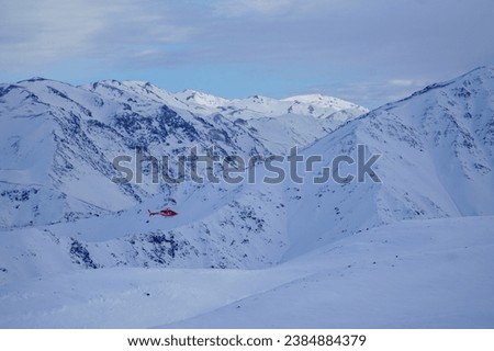 A helicopter traverses above the snow-capped mountains, soaring through the crisp alpine air.
