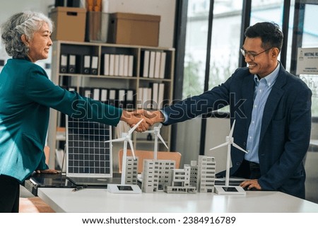 Shaking hands businesspeople professionals discuss renewable energy in office, showing solar panel, wind turbines with tower building model, apartment. modern business environmental, clean energy