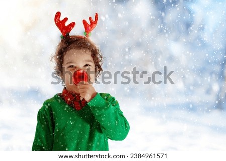 Child with reindeer nose and antlers on Christmas eve. Little boy holding a red bauble and Xmas present. Kids open Christmas gifts. Winter holiday fun. Family celebrating Christmas at home.
