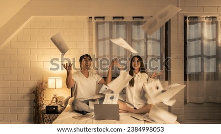 as asian couple throws financial graphs and business reports papers in the air, celebrating achievements in their cozy home office at night. Royalty-Free Stock Photo #2384998053