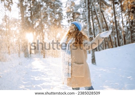 A young woman throws out snow. Portrait of a happy woman playing with snow on a sunny winter day. A walk through the winter forest. Concept of fun, relaxation. Royalty-Free Stock Photo #2385028509