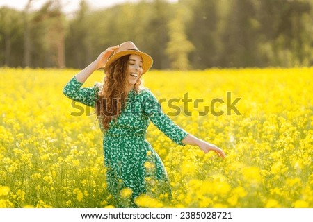 A happy woman in a hat walks through a blooming rapeseed field. Beautiful woman posing in a rapeseed field on a sunny day. Concept of nature, relaxation.