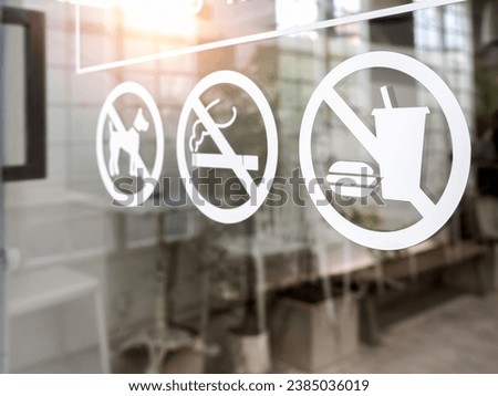 Close-up of no food and drink icon, pet and no smoking forbidden sign, white sticker on glass front door of cafe or restaurant.