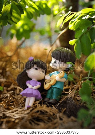 Romantic scene with dolls to Valentine's day. Representing a boy playing the guitar for a girl lying on dry autumn leaves in an artificial forest.  They are happy and in love.