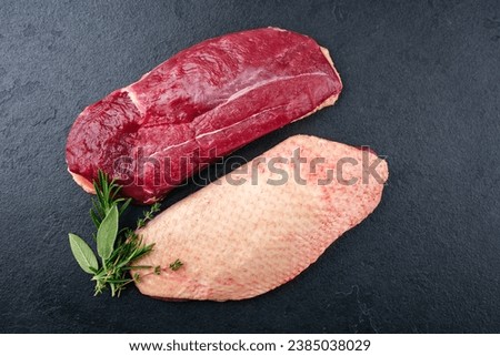 Traditional raw gourmet duck breast filet with skin offered with herbs as top view on a black board 