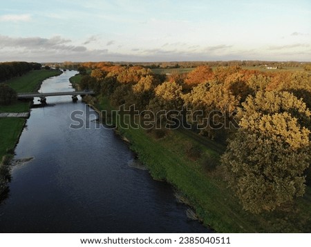 Dutch dike with bridge surrounded by autumn trees from aerial view during sunset
