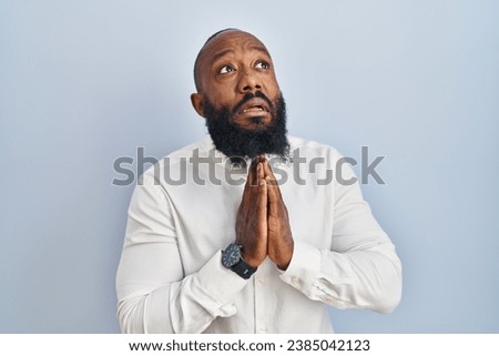African american man standing over blue background begging and praying with hands together with hope expression on face very emotional and worried. begging. 
