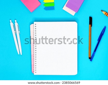 Top view flat lay blank blank checkered notebook with pens, stickers, bookmarks on blue background, design concept: spiral checkered notebook, isolated, place for text and design, mockup