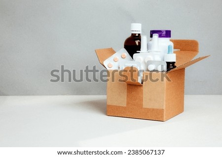 A set of medicines for treatment in bottles and tablets in transparent plates in a square cardboard box on a light background. Delivery of medicines. Front view Royalty-Free Stock Photo #2385067137