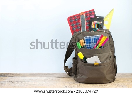 Backpack with different colorful stationery on table. White background. Back to school